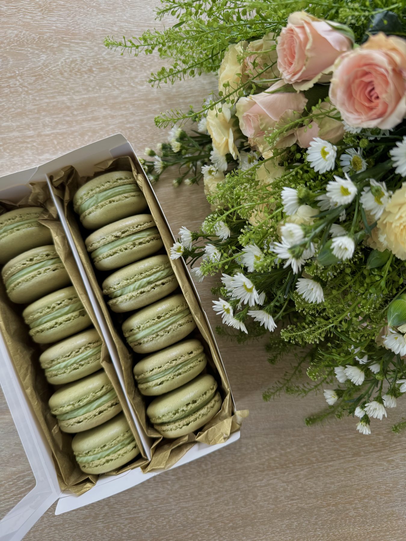 Matcha macarons boxed alongside fresh flowers